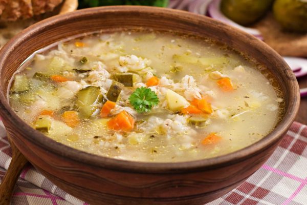 Soup with pickled cucumbers and pearl barley - rassolnik on a wooden background.