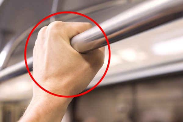 A man's hand holds on to the rail in the subway