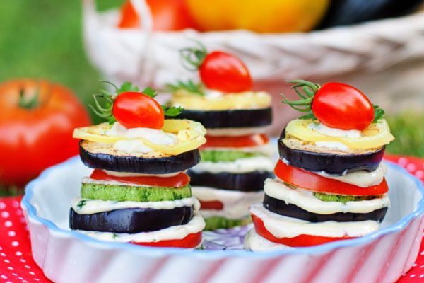 Tasty vegetable appetizer of tomatoes, eggplant, zucchini and white sauce on the background of the basket with ripe vegetables