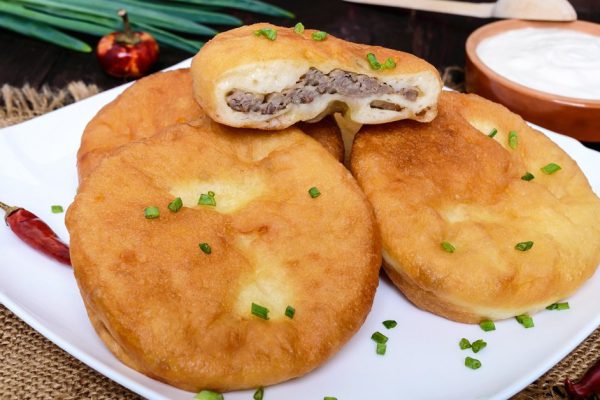 Deep frying pies with meat on a white plate with sour cream on dark wooden background.