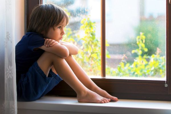 Sad child, boy, sitting on a window shield, watching the sunset