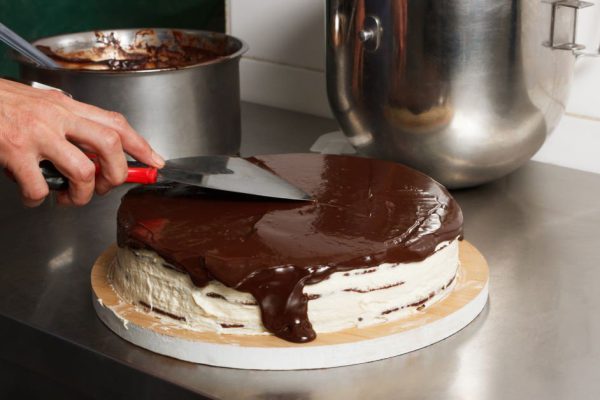 Woman smears chocolate cake with glaze icing, final stage of cooking. The process of making the chocolate cake, from begin to the end. Made by hands for confectionery.