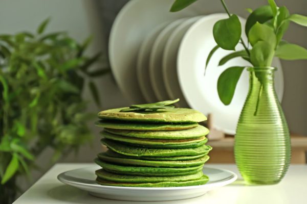 Plate with tasty green pancakes on table in kitchen