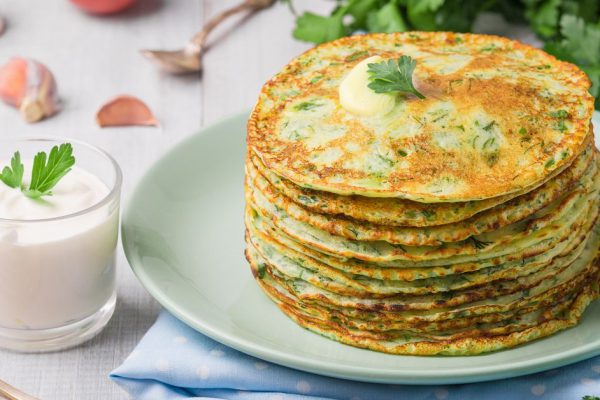 Many pancakes with fresh herbs and sour cream sauce on a wooden table. Traditional Ukrainian or Russian pancakes. Maslenitsa. Traditional dishes on the holiday Carnival Maslenitsa Shrovetide.