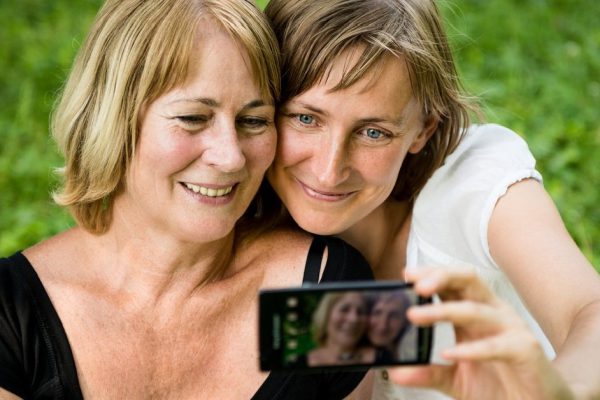 Adult daughter and her senior mother are taking picture with mobile phone