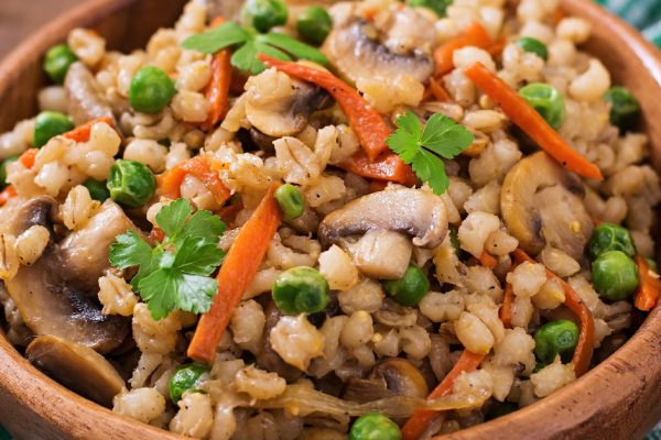 Vegetarian crumbly pearl barley porridge with mushrooms and green peas in a wooden bowl