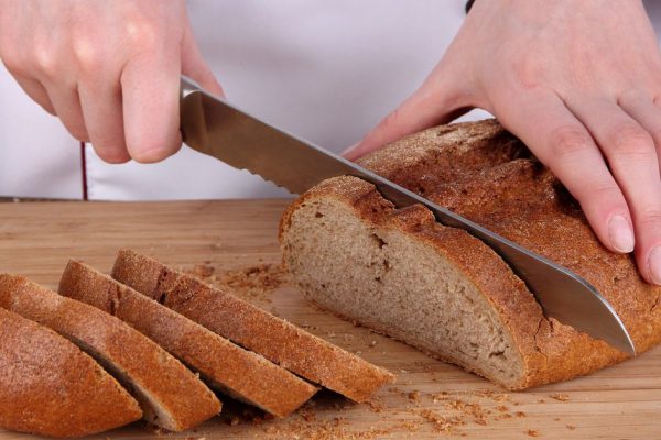 Cutting bread on wooden board close up