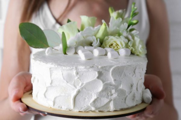 Woman holding cake decorated with marshmallows and flowers