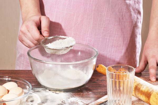 The man's hand sifts a flour in a cup through a sieve