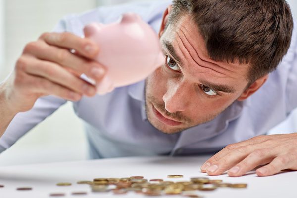 business, people, finances, crisis and money saving concept - businessman shaking piggy bank and getting coins at office
