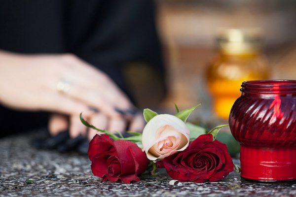 Woman in mourning arranging flowers and candles on the gravestone