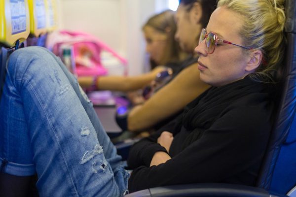 People flying by plane. Interior of airplane with passengers sleeping on seats. Tired woman napping on uncomfortable seat on airplane. Commercial transportation by planes.