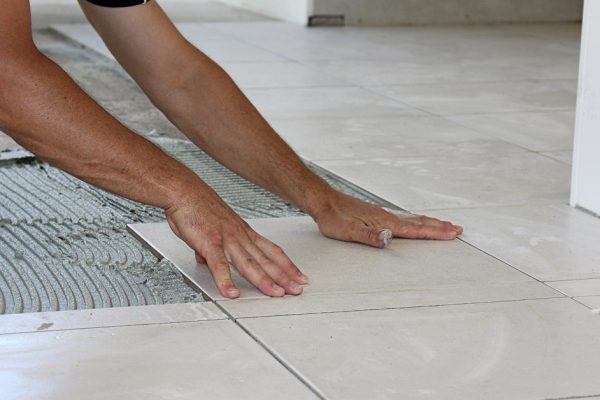 a male tiler laying light color floor tiles
