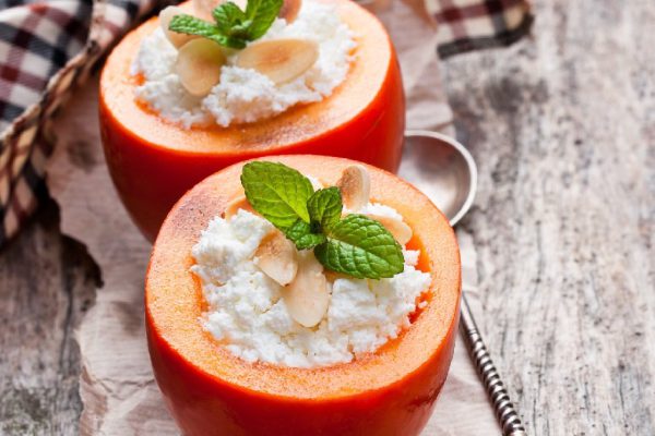 Sweet  persimmons stuffed with cottage cheese and almonds on wooden table