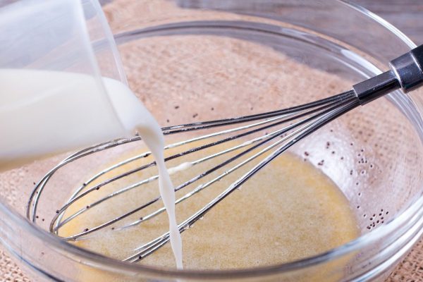 Mixing dough on kitchen table background with cooking ingredients ad add milk. Pastry making