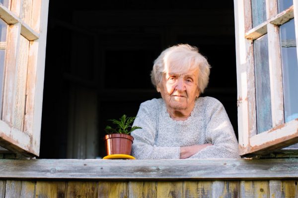 Elderly woman looks from window of a village house.