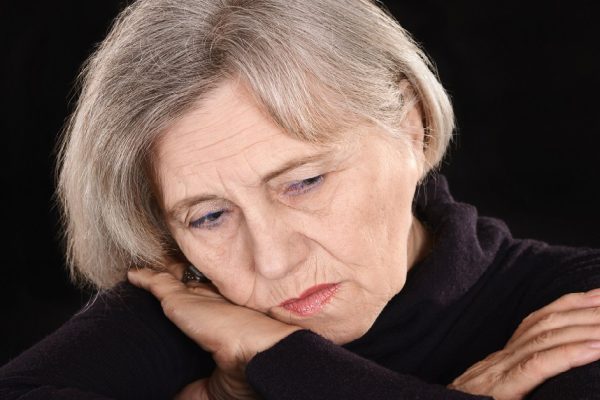 melancholy senior woman thinking on a black background