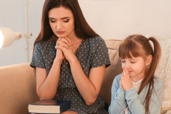 Religious Christian girl and her mother praying at home