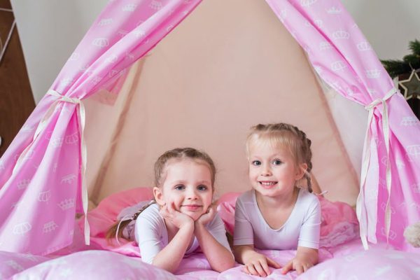 Two little girls, sisters, friends play in a tent in a house or teepee.