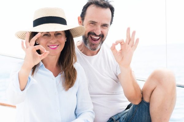 Middle age couple traveling on sailboat doing ok sign with fingers, excellent symbol