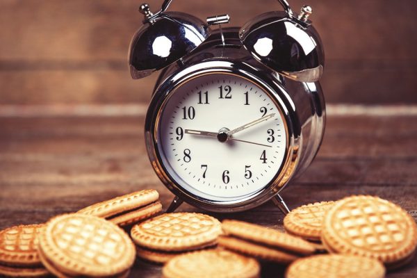 Retro alarm clock with cookie on a table. Photo in retro color image style