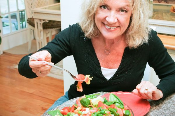 Fit, sexy senior woman eating a tossed green salad in her lovely modern home.
