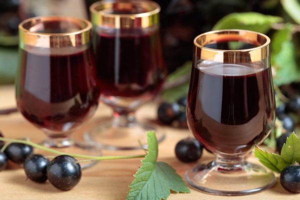 Homemade black currant liqueur and fresh berries on a branch , wooden background.
