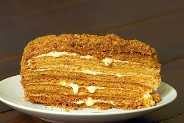 Honey layered piece of cake on white plate on wooden table