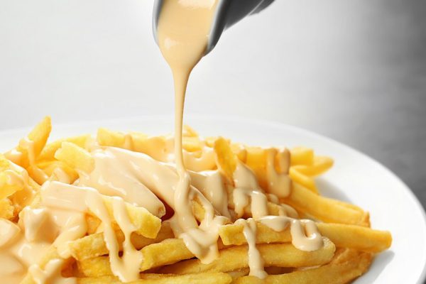 Pouring cheese sauce on french fries, closeup