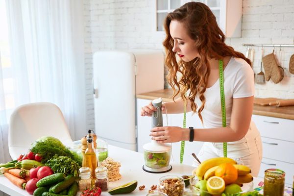 Young happy woman preparing tasty salad in the beautiful kitchen with green fresh ingredients indoors. Healthy food and Dieting concept. Loosing Weight