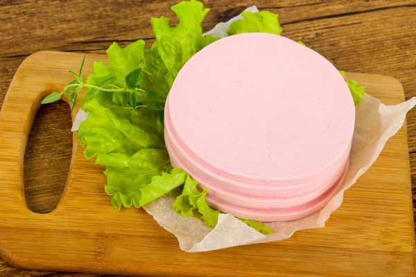 Sliced sausage with salad leaves over the wooden background