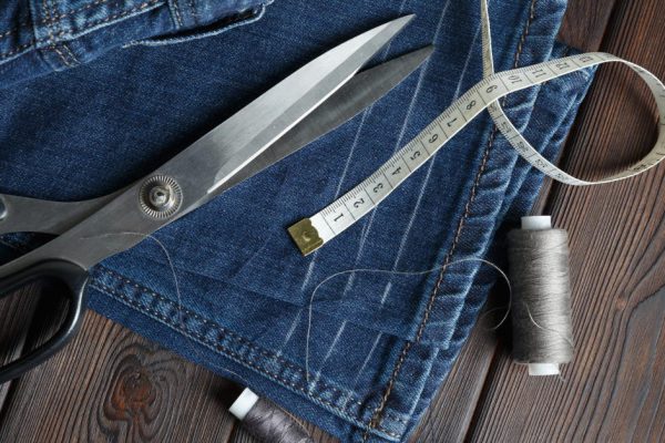 Jeans with dressmaking sewing utensils needlework on the dark old wood background