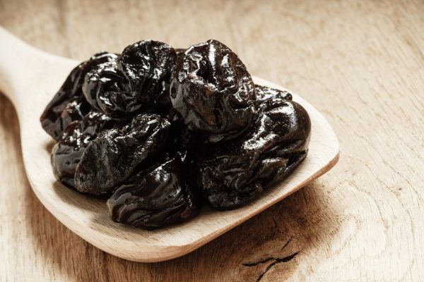 Healthy food, good cuisine. Closeup dried plums prunes fruits on wooden spoon rustic table background