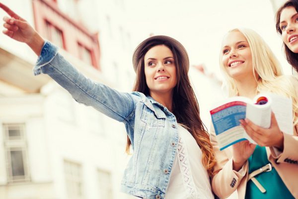 holidays and tourism concept - beautiful girls looking for direction in the city