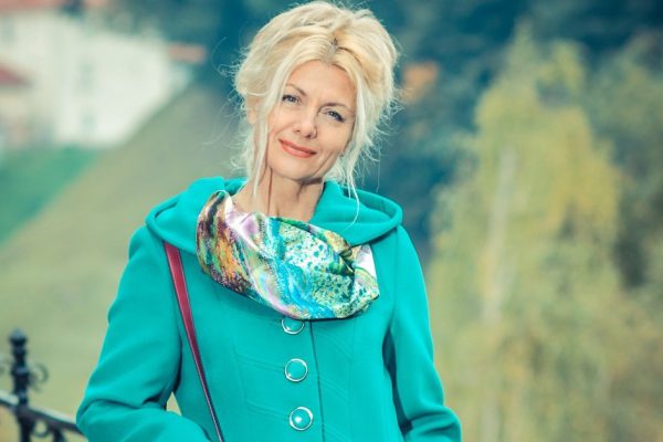 Beautiful mature blonde in  coat posing in the park. Portrait of a senior woman outdoors.