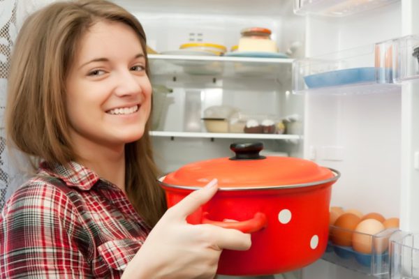 Teenager girl putting pan into fridge  at home