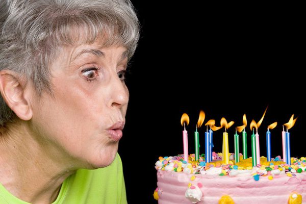 A senior female blows out candels on a cake.  Ideal for birthday, anniversary or any other celebration inference.