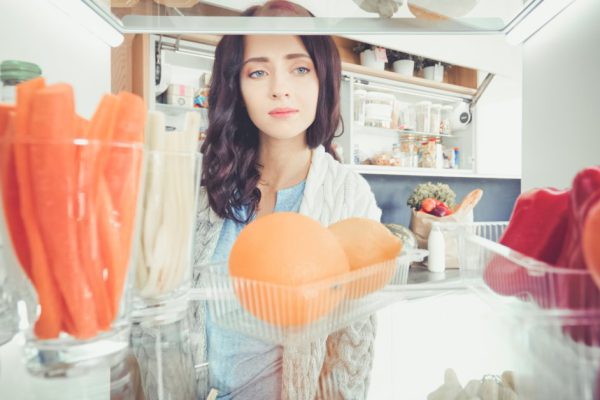 Portrait of female standing near open fridge full of healthy food, vegetables and fruits. Portrait of female.