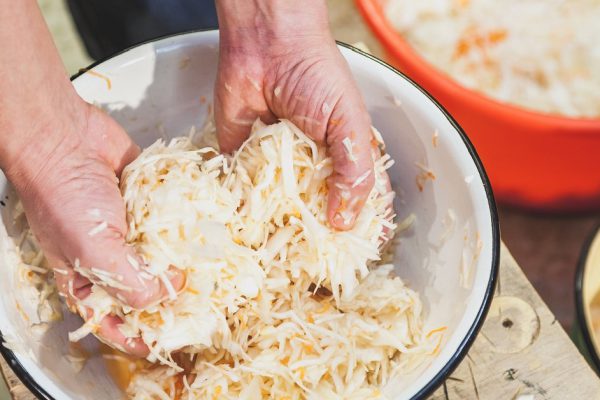 Preparation of salted cabbage at home. Hands wrinkle shredded white cabbage in a round bowl