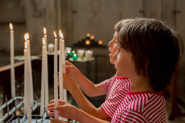 Little boy prays and puts a candle in Orthodox Church, sad kid with faith