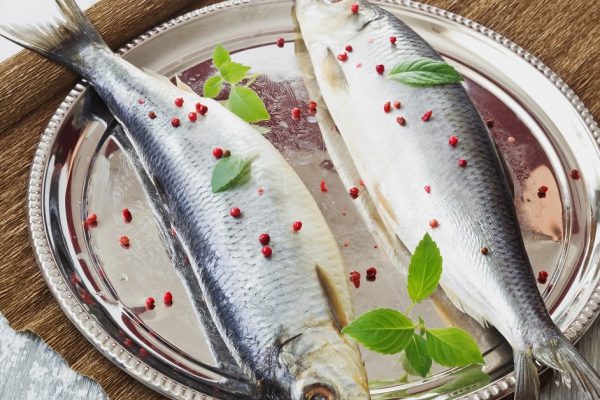 salted herring with spices in an iron dish on a wooden table. healthy sea food