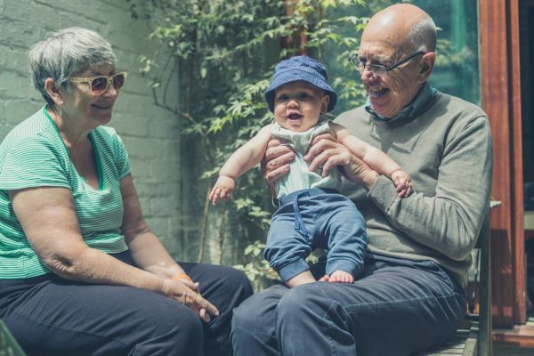 A little baby is playing with his grandparents in the backyard on a summer day