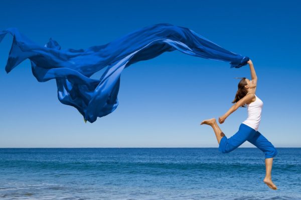 Beautiful young woman jumping on the beach with a colored tissue