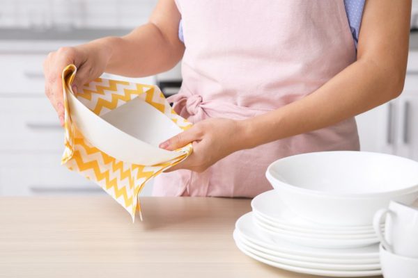 Woman wiping clean dish at table in kitchen, closeup