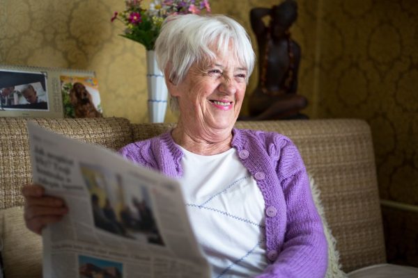 Senior woman reading morning newspaper, sitting in her favorite chair in her living room, looking happy