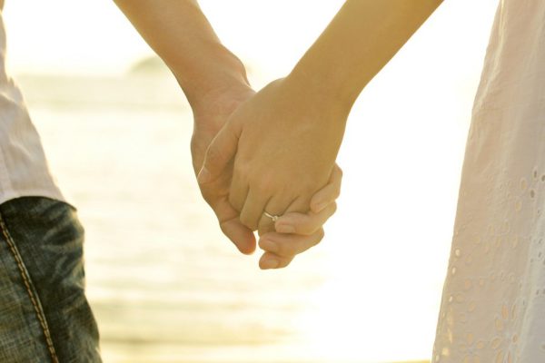 Young adult male and female holding hands on beach at sunset.