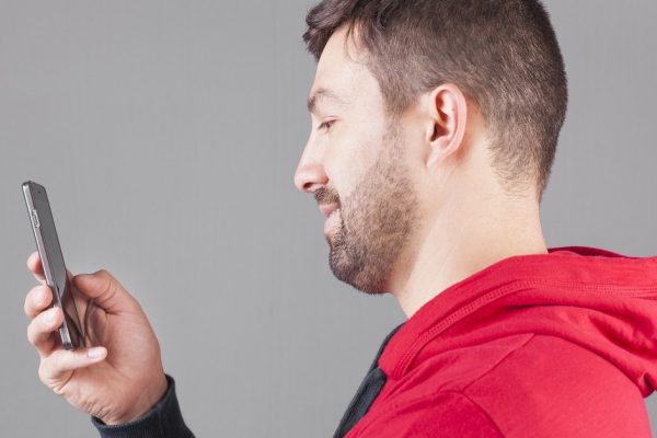 Smiling young man text messaging on his smart phone
