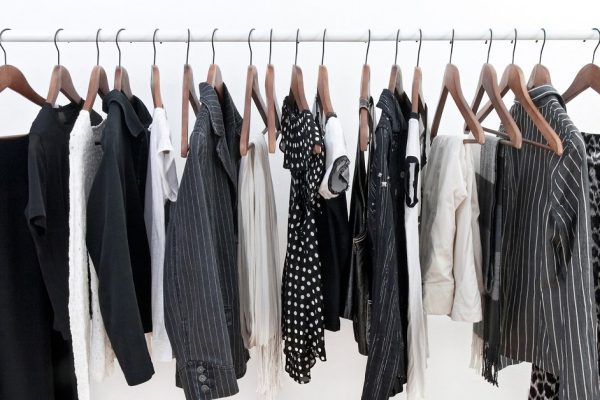 Female black and white clothes on a rod and shoes on a wooden floor.