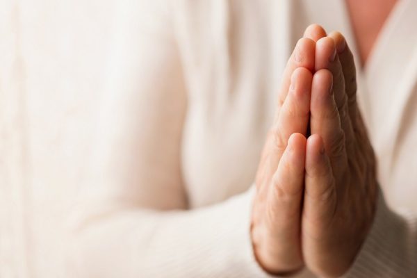 Hands of an unrecognizable woman in white cardigan praying