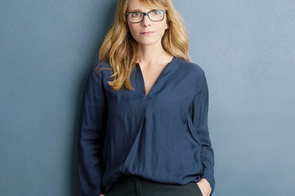 Shot of a beautiful confident woman looking at camera and smiling while standing by the wall.